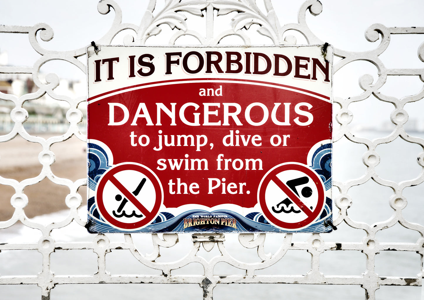 Warning sign on a decorative white metal fence, stating 'It is forbidden and dangerous to jump, dive or swim from the pier.' Palace Pier limited edition print By Stef Kerswell